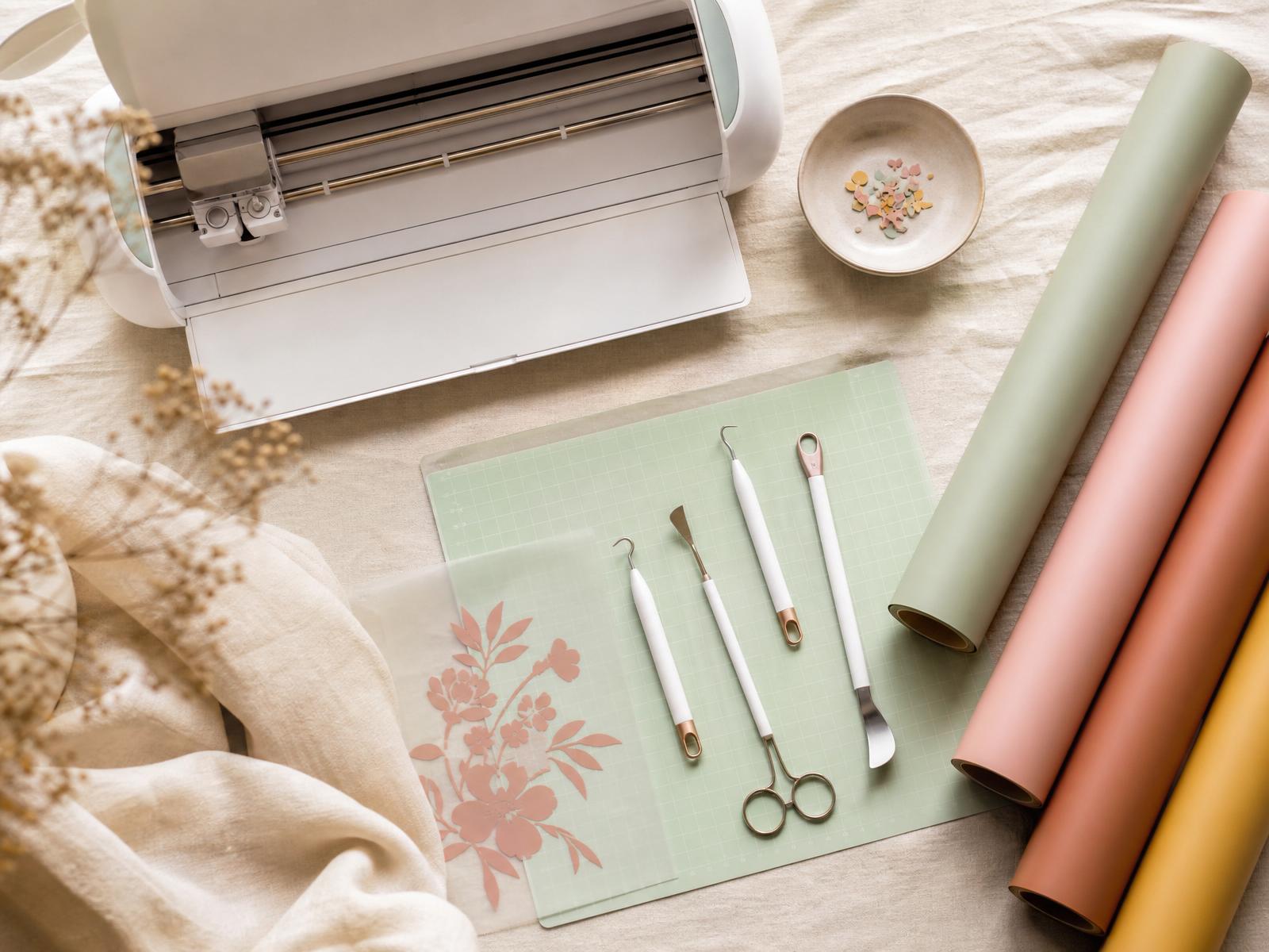 Cricut cutting machine surrounded by pastel vinyl rolls and rose gold tools